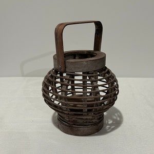 May include: A brown woven lantern with a handle. The lantern is made of natural materials and has a rustic look.