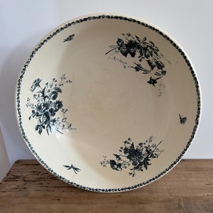 May include: A large, white ceramic bowl with a blue floral pattern. The bowl has a scalloped edge and is decorated with delicate blue flowers, leaves, and butterflies.