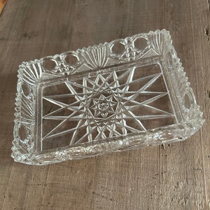 May include: A clear glass serving tray with a starburst pattern in the center and a scalloped edge.