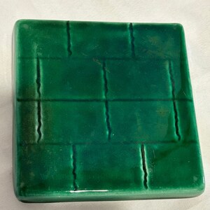 Può includere: Una piastrella quadrata in ceramica verde con un motivo intrecciato in rilievo.