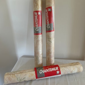 以下が含まれることがあります： 3つの壁紙ロールが表示されています。2つは直立しており、1つは水平です。壁紙はクリーム色とベージュの花柄です。各ロールには「CHANTEMUR」という赤いラベルが付いています。サイズ：53 cm x 10 m.