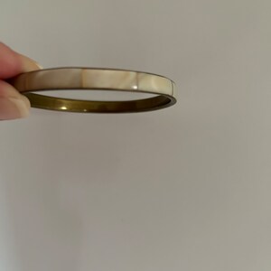 Könnte beinhalten: Ein weißes und goldenes Armreif-Armband mit einem Perlmutteinlege.
