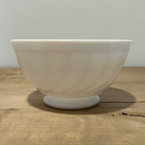 Può includere: Una ciotola in ceramica bianca con un bordo scanalato e un design a spirale. La ciotola ha una base arrotondata.