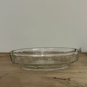 Op de afbeelding: Een heldere, ovaalvormige glazen serveerschaal met een geometrisch ontwerp. De schaal heeft een laag profiel en staat op een houten oppervlak. De schaal wordt waarschijnlijk gebruikt voor het serveren van voedsel.
