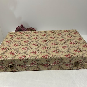 May include: A rectangular box with a floral pattern in red and beige. The box has a hinged lid and metal clasps. The floral design features roses and leaves.