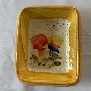 Könnte beinhalten: Eine kleine, rechteckige Keramikschale mit gelber Glasur und einem Blumendesign. Die Schale hat einen erhöhten Rand und eine gesprenkelte Glasur.