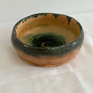 Peut inclure: Un bol rond en céramique avec un glaçage vert et brun. Le bol a un bord légèrement irrégulier et une surface texturée.
