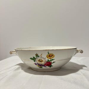 Op de afbeelding: Een witte keramische serveerschaal met twee handvatten. De schaal heeft een bloemenmotief met gele, rode, witte en paarse bloemen.