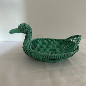 Könnte beinhalten: Ein blaugrüner Korb aus Weidengeflecht in Form einer Ente. Der Korb ist mit einer feinen Webart geflochten und hat einen langen Hals und einen kleinen Schnabel.