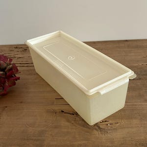 Puede incluir: Un recipiente de almacenamiento rectangular de plástico blanco con tapa. El recipiente está sobre una superficie de madera.