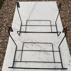 Peut inclure: Deux supports en fil métallique noir avec une base rectangulaire et quatre bras de support incurvés vers le haut. Chaque support présente une conception simple à cadre ouvert construite à partir de fines tiges métalliques sombres.