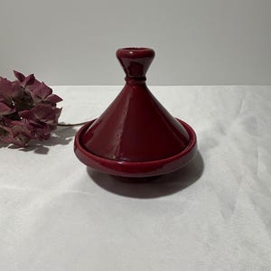 May include: A deep red ceramic tagine with a conical lid. The tagine is a traditional Moroccan cooking pot.