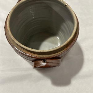K&ouml;nnte beinhalten: Eine braune Keramik-Dose mit Deckel und Henkel. Die Dose hat ein glasiertes Inneres und eine strukturierte Au&szlig;enseite.