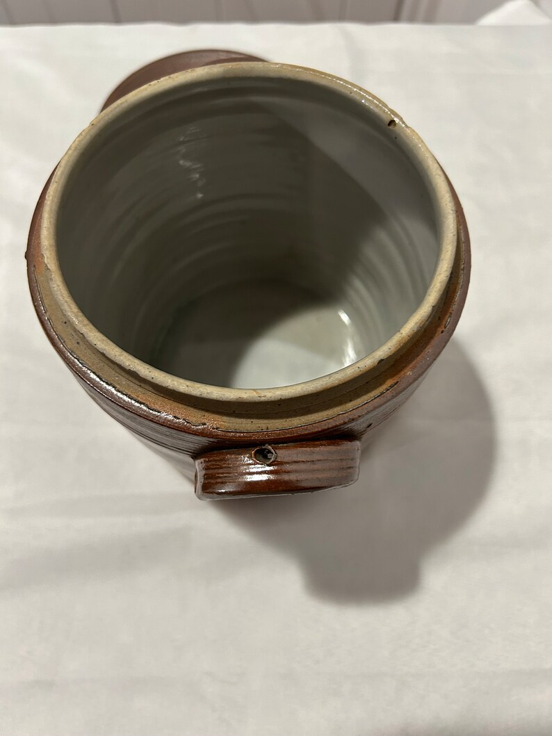 K&ouml;nnte beinhalten: Eine braune Keramik-Dose mit Deckel und Henkel. Die Dose hat ein glasiertes Inneres und eine strukturierte Au&szlig;enseite.