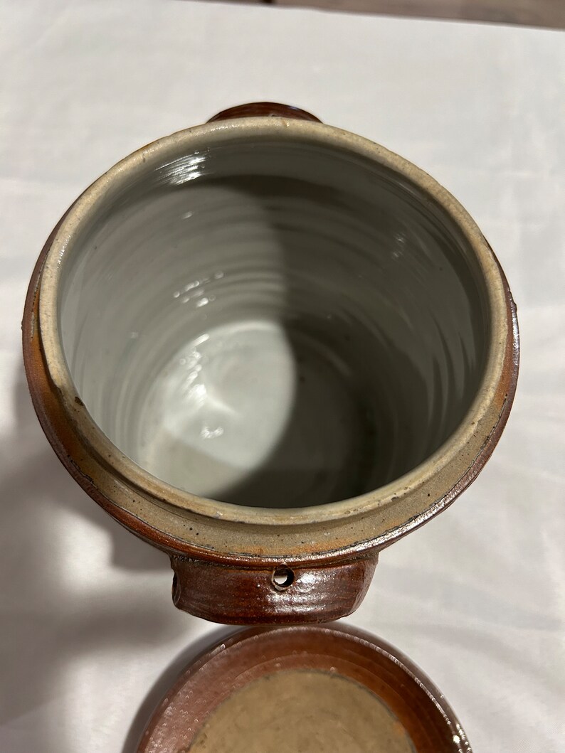 K&ouml;nnte beinhalten: Eine braune Keramik-Dose mit Deckel. Die Dose hat zwei Griffe und ein kleines Loch an der Seite. Der Deckel ist ebenfalls braun und hat ein kleines Loch in der Mitte.