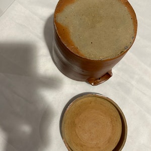 K&ouml;nnte beinhalten: Ein brauner Keramiktopf mit Deckel. Der Topf hat eine raue, strukturierte Oberfl&auml;che und der Deckel ist glatt. Der Topf ist leer.