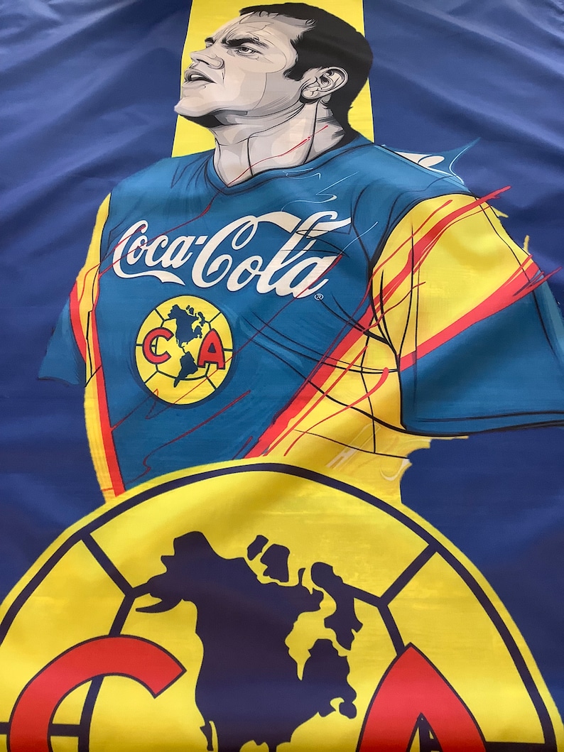 May include: A blue and yellow soccer jersey with the text "Coca-Cola" and a logo of a world map with the letters "CA" inside. The jersey is worn by a cartoon illustration of a soccer player.