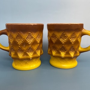 May include: Two ceramic mugs with a textured diamond pattern. The mugs have a yellow base and handle, with a brown rim and diamond pattern. The mugs are suitable for coffee, tea, or other beverages.