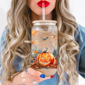Puede incluir: Un vaso de vidrio transparente con un dise&ntilde;o de Halloween en negro, naranja y marr&oacute;n que presenta una calabaza y murci&eacute;lagos. El vaso tiene una tapa de bamb&uacute; y una pajita.