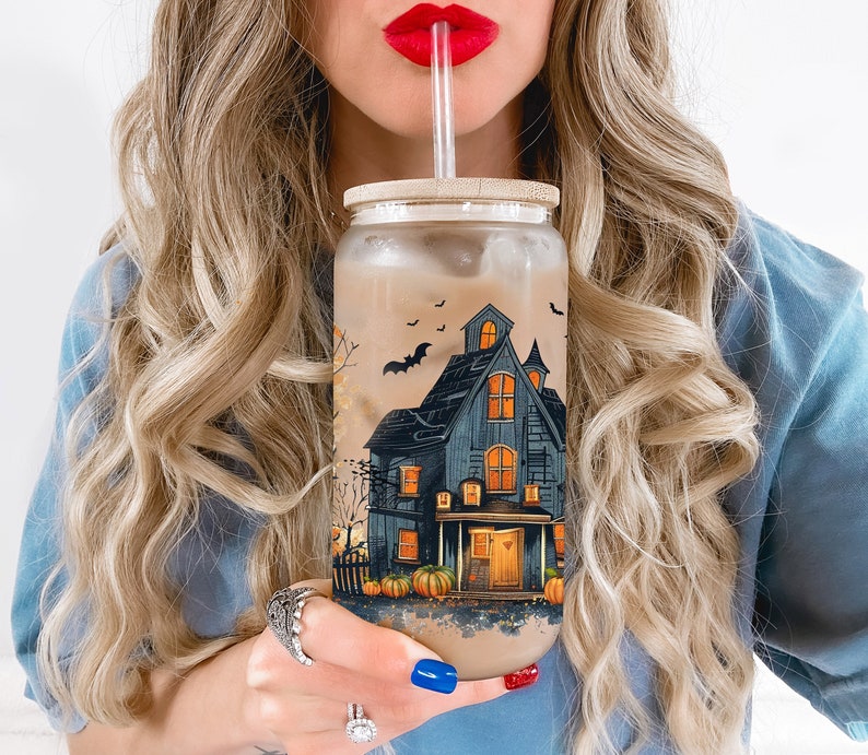 Peut inclure: Un gobelet en verre transparent avec un motif d'Halloween effrayant repr&eacute;sentant une maison hant&eacute;e, des chauves-souris et des citrouilles. Le gobelet est rempli d'un liquide brun et est muni d'une paille.