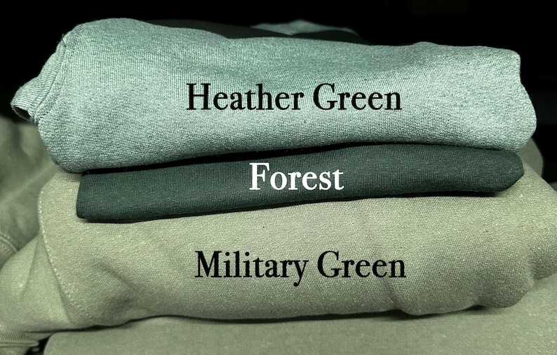 May include: A stack of three folded sweatshirts in shades of green. The top sweatshirt is heather green, the middle is forest green, and the bottom is military green. Text labels each color.