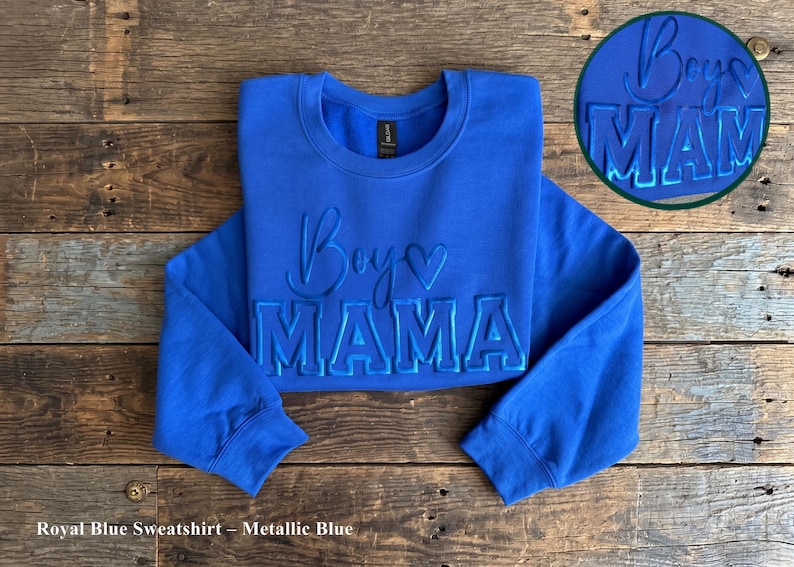May include: Royal blue sweatshirt with the words "Boys Mama" in metallic blue lettering. The sweatshirt has a crew neck and long sleeves. A circular graphic with the same text is in the upper right corner.