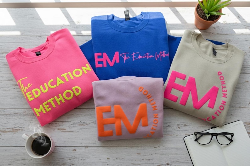 May include: Four sweatshirts in pink, blue, lavender, and beige, each with a different color of text. The pink sweatshirt has the words "The EDUCATION METHOD" in yellow. The blue sweatshirt has "EM The Education Method" in pink.