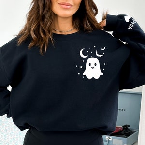 Puede incluir: Sudadera negra con un fantasma blanco, una luna creciente, estrellas y murci&eacute;lagos. La manga tiene la palabra "OPHIA" impresa.