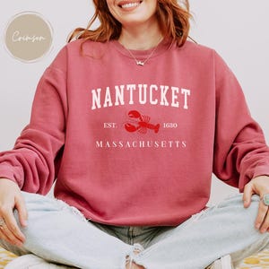 May include: Crimson-colored sweatshirt with the word "Nantucket" in white block letters, a red lobster graphic, and the text "Est. 1630 Massachusetts." The sweatshirt has long sleeves and a crew neck.