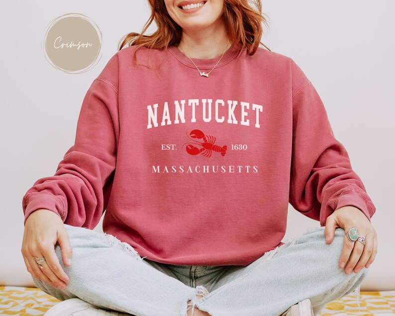 May include: Crimson-colored sweatshirt with the word "Nantucket" in white block letters, a red lobster graphic, and the text "Est. 1630 Massachusetts." The sweatshirt has long sleeves and a crew neck.
