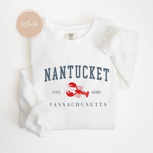 May include: White sweatshirt with the word "Nantucket" in navy blue block letters, a red lobster graphic, and the text "EST. 1630 Massachusetts". The sweatshirt has long sleeves and a crew neck.