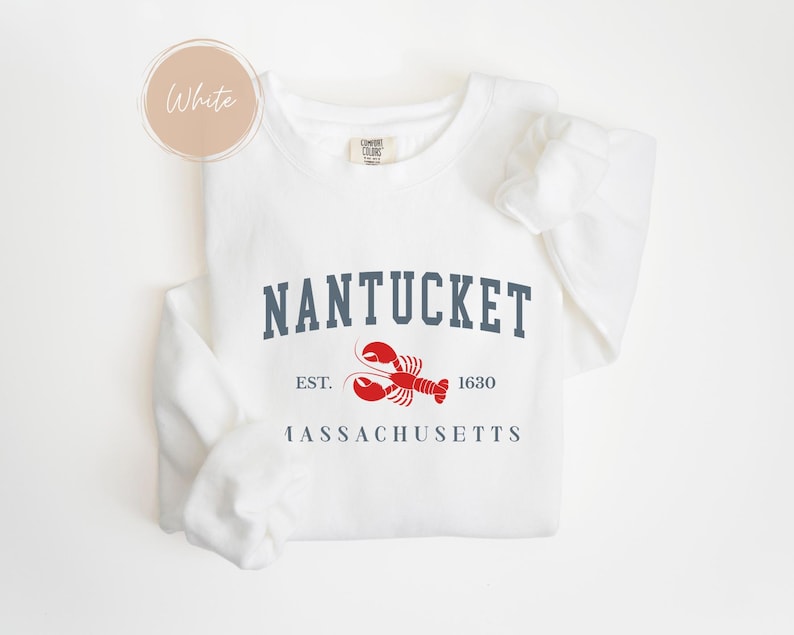 May include: White sweatshirt with the word "Nantucket" in navy blue block letters, a red lobster graphic, and the text "EST. 1630 Massachusetts". The sweatshirt has long sleeves and a crew neck.