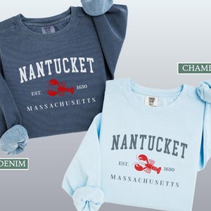 May include: Two crewneck sweatshirts, one denim blue and one chambray blue, with the word "NANTUCKET" in white block letters. Below the word is a red lobster graphic and the text "EST. 1630 MASSACHUSETTS".