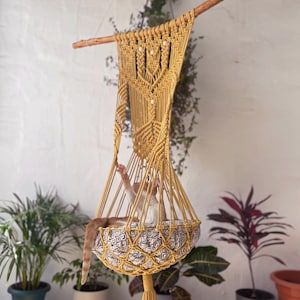 May include: A yellow macrame cat hammock with a patterned cushion. Two cats are relaxing in the hammock.