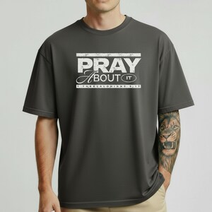 Puede incluir: Camiseta gris oscuro con el texto blanco "PRAY About IT" y la referencia bíblica "1 Thessalonians 5:17" debajo. La camiseta es de color liso y tiene mangas cortas.