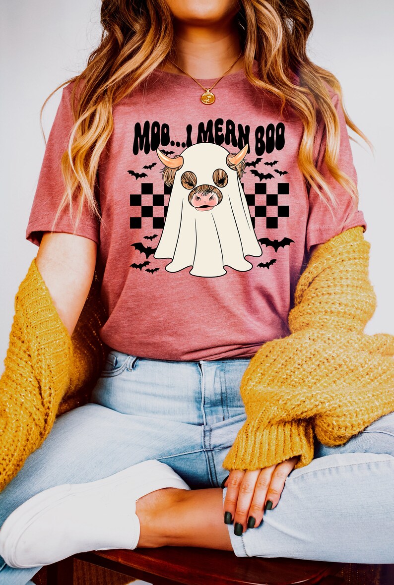 May include: A pink t-shirt with a graphic of a Highland cow dressed as a ghost. The text "Moo...I mean Boo" is printed on the shirt.