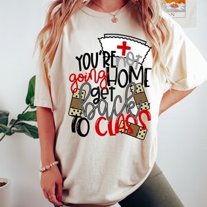 May include: A white t-shirt with a red and black graphic that says "You're not going home get back to class". The graphic includes a nurse's cap with a red cross and band-aid designs.