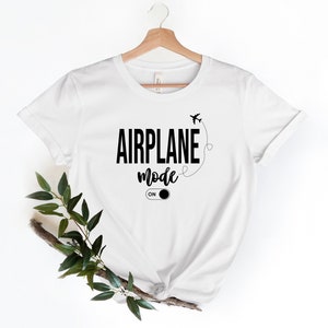 May include: White t-shirt with black text that reads "Airplane Mode On" with a stylised airplane and an on/off switch graphic.