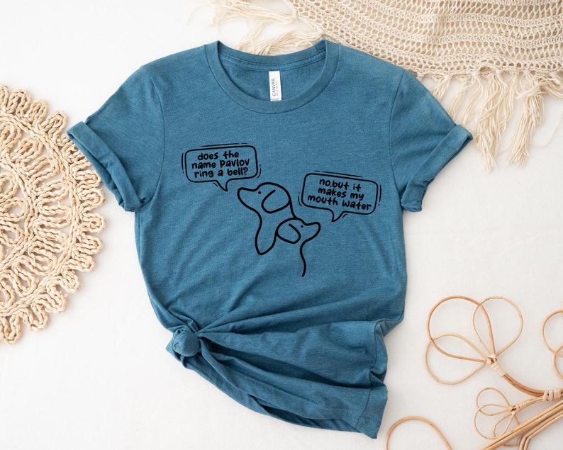 May include: A teal blue t-shirt with a black graphic of two dogs and text that reads "does the name Pavlov ring a bell? no but it makes my mouth water."