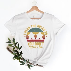 May include: White t-shirt with a vintage-style graphic that says "I read the rules so you don't have to". The graphic features a sunset with two figures in silhouette.
