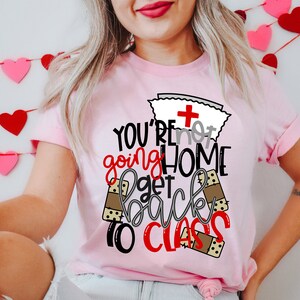 May include: Pink t-shirt with a nurse's cap and the text "You're not going home get back to class" with band-aid graphics.