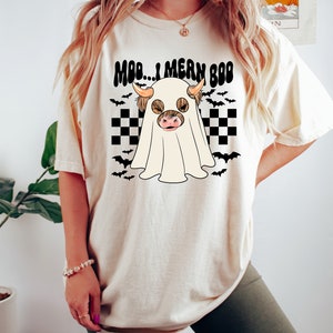May include: A white t-shirt with a black and white checkered pattern and a ghost with a cow's head. The text on the shirt reads "Moo... I mean Boo".
