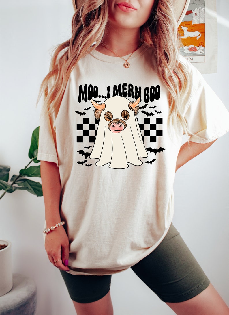 May include: A white t-shirt with a black and white checkered pattern and a ghost with a cow's head. The text on the shirt reads "Moo... I mean Boo".