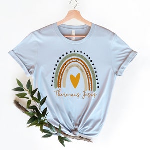 May include: Light blue t-shirt with a rainbow design and the text "In the waiting, in the searching, in the healing, in the hurting, every minute, every moment, there was Jesus".