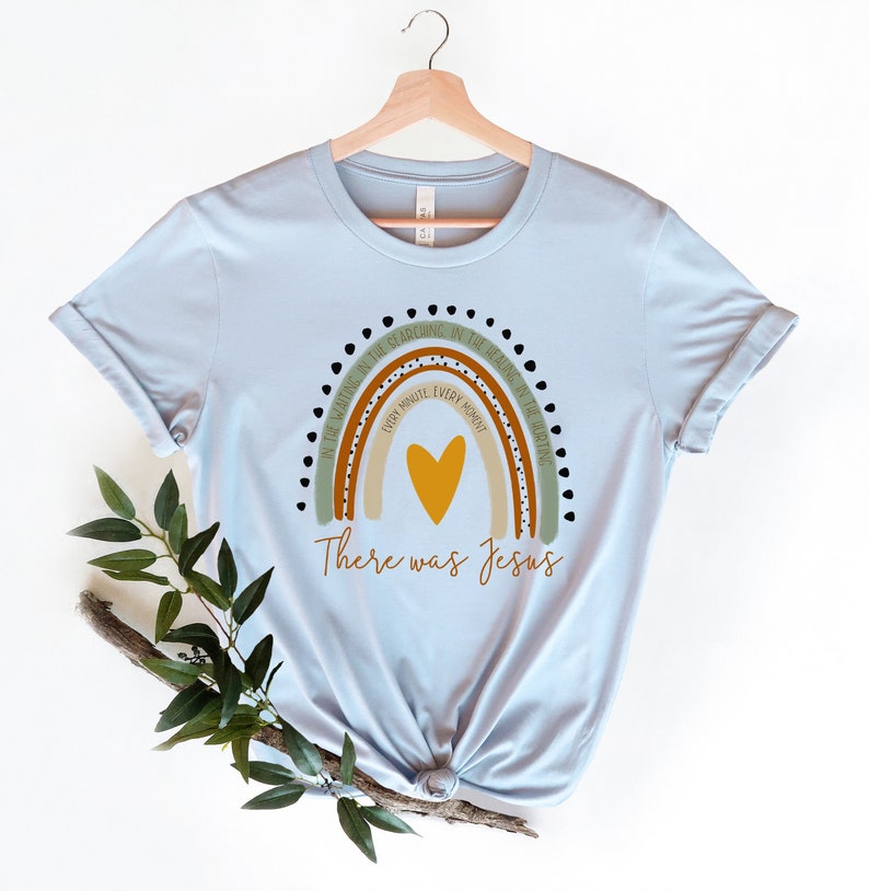 May include: Light blue t-shirt with a rainbow design and the text "In the waiting, in the searching, in the healing, in the hurting, every minute, every moment, there was Jesus".