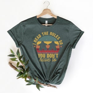 May include: A dark green t-shirt with a vintage-style graphic that says "I read the rules so you don't have to". The graphic features a sunset with three figures in silhouette.
