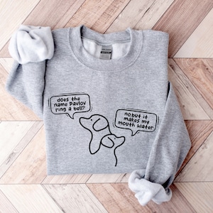 May include: Gray sweatshirt with a black and white illustration of two dogs. The text on the sweatshirt reads "does the name Pavlov ring a bell?" and "no.but it makes my mouth water".