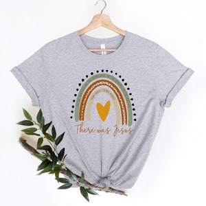 May include: A gray t-shirt with a rainbow design and the text "In the waiting, in the searching, in the healing in the hurting, every minute, every moment, there was Jesus".