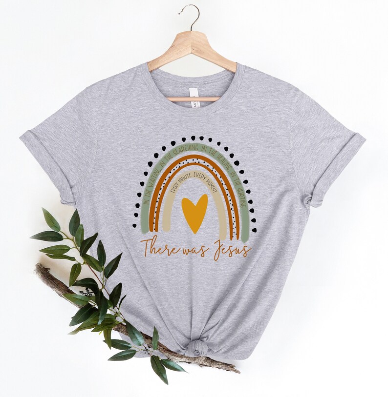 May include: A gray t-shirt with a rainbow design and the text "In the waiting, in the searching, in the healing in the hurting, every minute, every moment, there was Jesus".