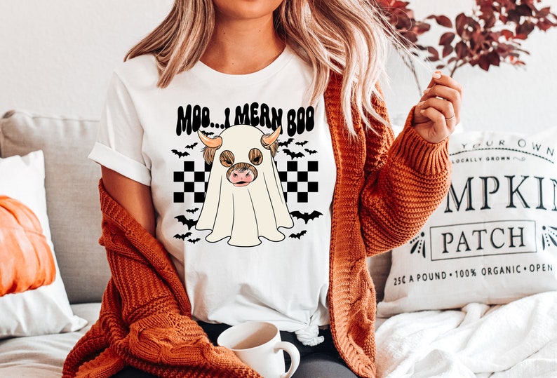 May include: White t-shirt with a black and white checkered background and a ghost with a brown and white cow head inside. The text "MOD... I MEAN BOO" is above the ghost.